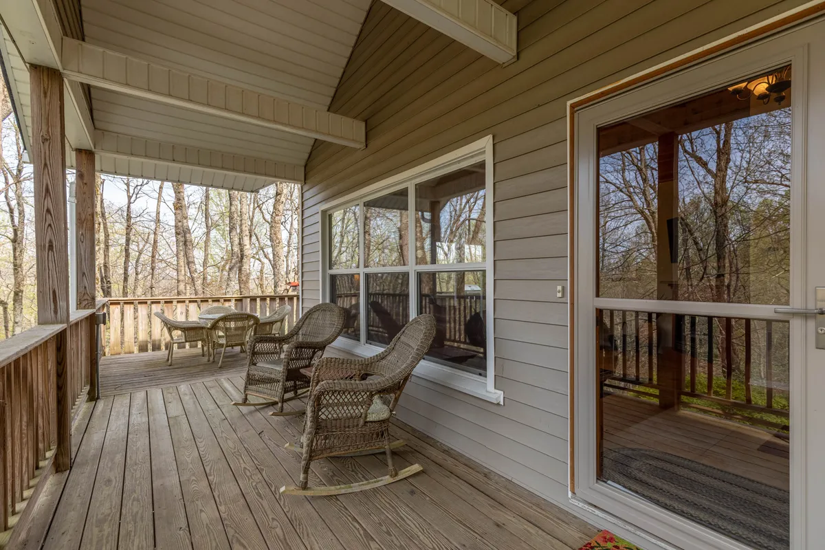 A serene sitting area with rocking chairs and a small outdoor table set beside expansive windows, offering views of the changing seasons outside. The warm wood elements and natural light create a tranquil atmosphere, perfect for enjoying a morning coffee or unwinding after a day exploring the mountains.