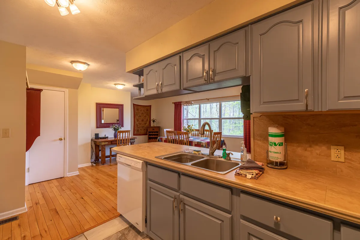 The kitchen island with a sink overlooks both the dining area and a window with a peaceful outdoor view. The image captures the seamless transition from meal preparation to dining, with natural light streaming in and a cozy, connected layout.
