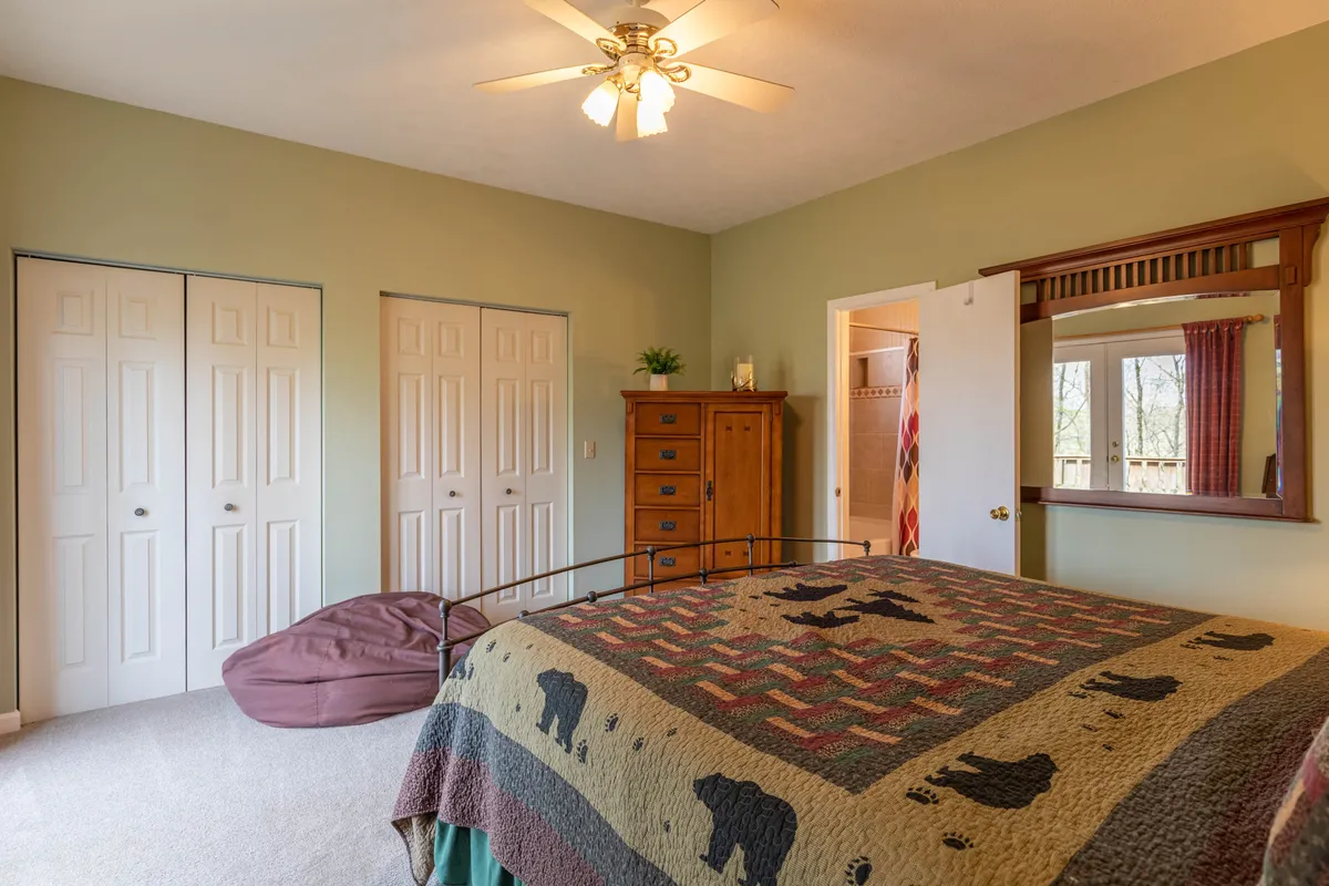 A cozy bedroom with a bed adorned in a patterned quilt, a wooden dresser, double closets, and a decorative mirror. The mood is relaxed and comfortable—perfect for guests seeking a serene space to rest and recharge.