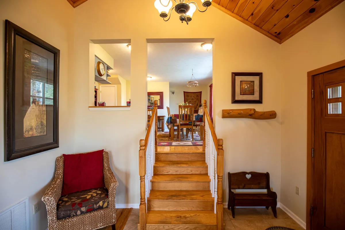 This image captures the entryway or main living space of the home, featuring a decorative staircase, a stylish chair, wall art, and a wooden bench. The space feels welcoming, bathed in natural light filtering through windows, and hints at a warm, inviting atmosphere.