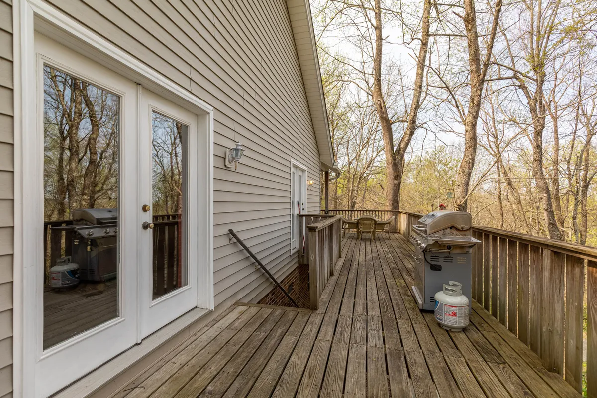 An inviting exterior deck space with a grill and seating area, set against the backdrop of surrounding trees. The image captures a relaxed mood suitable for barbecuing, gathering with friends, and enjoying the fresh mountain air.