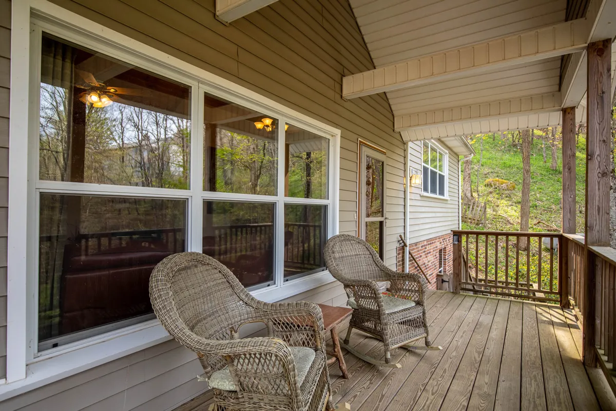 Wicker chairs arranged on a wooden deck outside, with large windows of the house in view and the forest as a tranquil backdrop. The scene evokes a peaceful atmosphere ideal for watching the sunrise or stargazing while listening to the sounds of the outdoors.